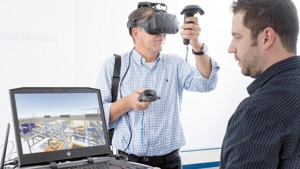 Virtuelle Welt: Dennis Heuser (rechts) zeigt einem Kunden, wie er mittels VR-Brille und Handgeräten die Abläufe in einem Lager steuern kann.